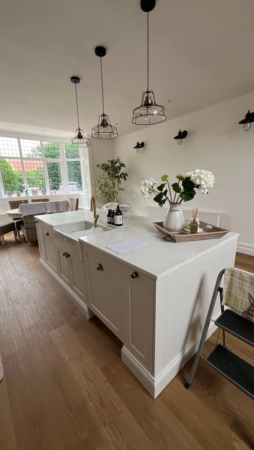 Kitchen island detail with a brass tap and Belfast-style sink, quartz worktop and dining area in the background