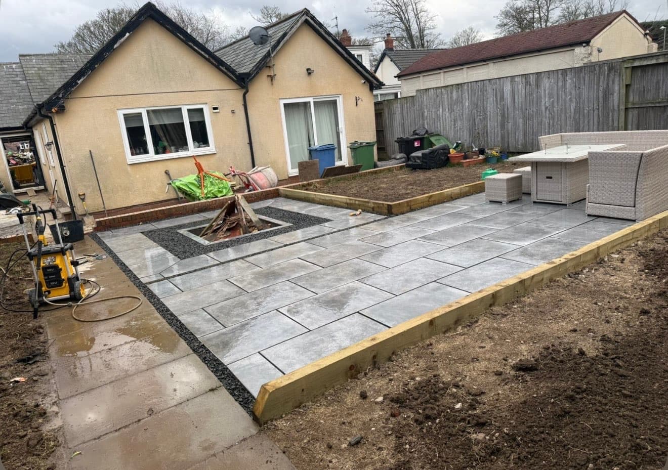 Grey porcelain-effect patio with sunken fire pit, viewed from ground level toward the house