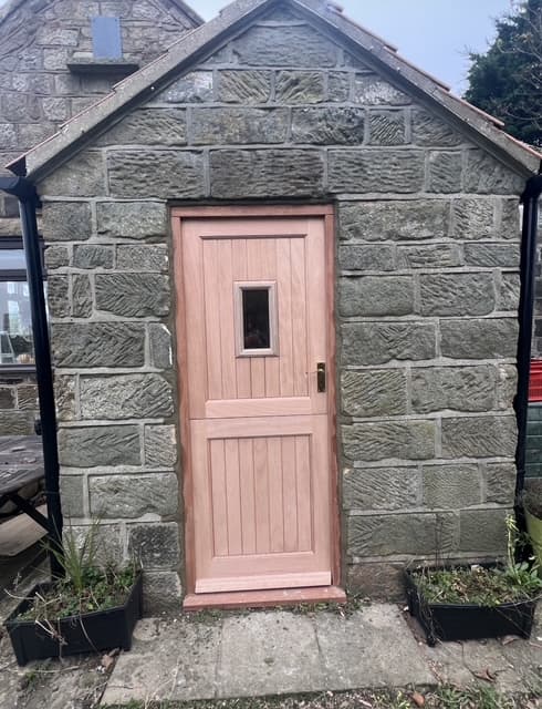 A new bespoke stable-style timber door being fitted into a stone-walled bay, shown unfinished before painting